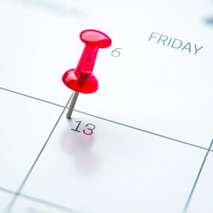 A red pushpin is stuck into a calendar on Friday the 13th, highlighting an important date.
