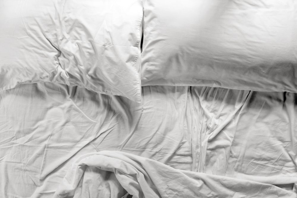 Flat lay view of an unmade bed in a bedroom with two pillows and crumpled bed sheet, after waking up in the morning. Couple lifestyle concept. copy space