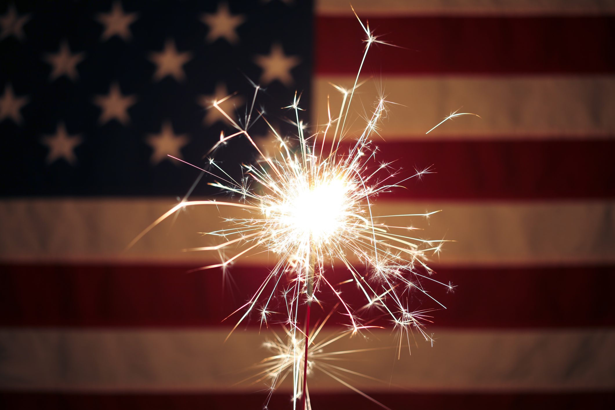 Lit sparkler in front the American Flag for 4th of July celebration