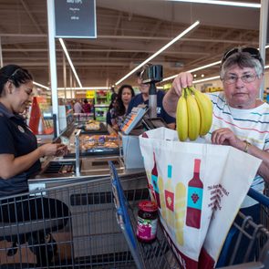 Cashier (left) sitting down at an Aldi checkout line while a customer puts bananas into a grocery bag