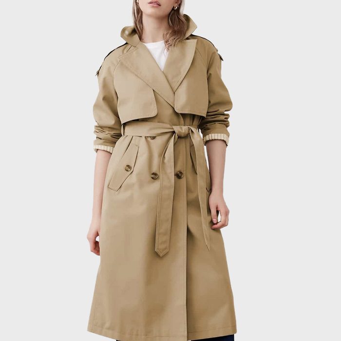 A woman stands in a classic trench coat with a belt