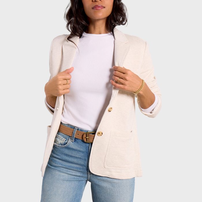 A woman wears a Blazer in a soft cotton blend over a white shirt, light blue jeans, and a brown belt holding the blazer slightly open.