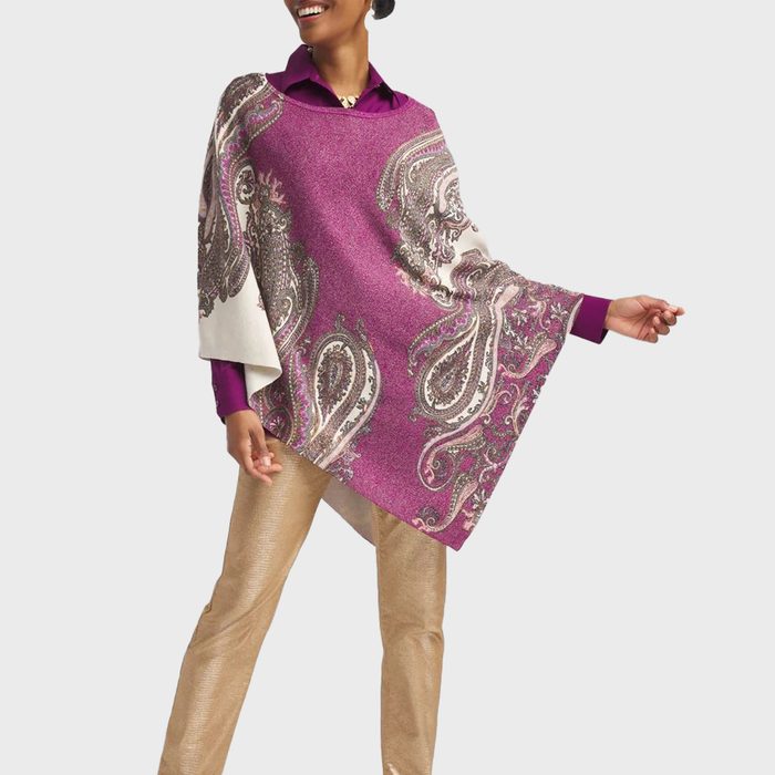 A woman wearing a purple blouse, a paisley-patterned purple poncho, gold pants