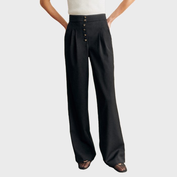 A person wearing Cesar Trousers—high-waisted, wide-leg black pants with pleats and five buttons and heeled sandals