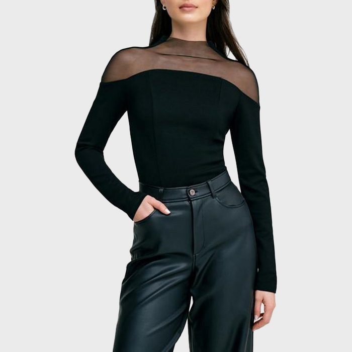 A woman poses in the Marcella Women's Joanna Top—black with sheer mesh shoulders and long sleeves—paired with high-waisted black leather pants.